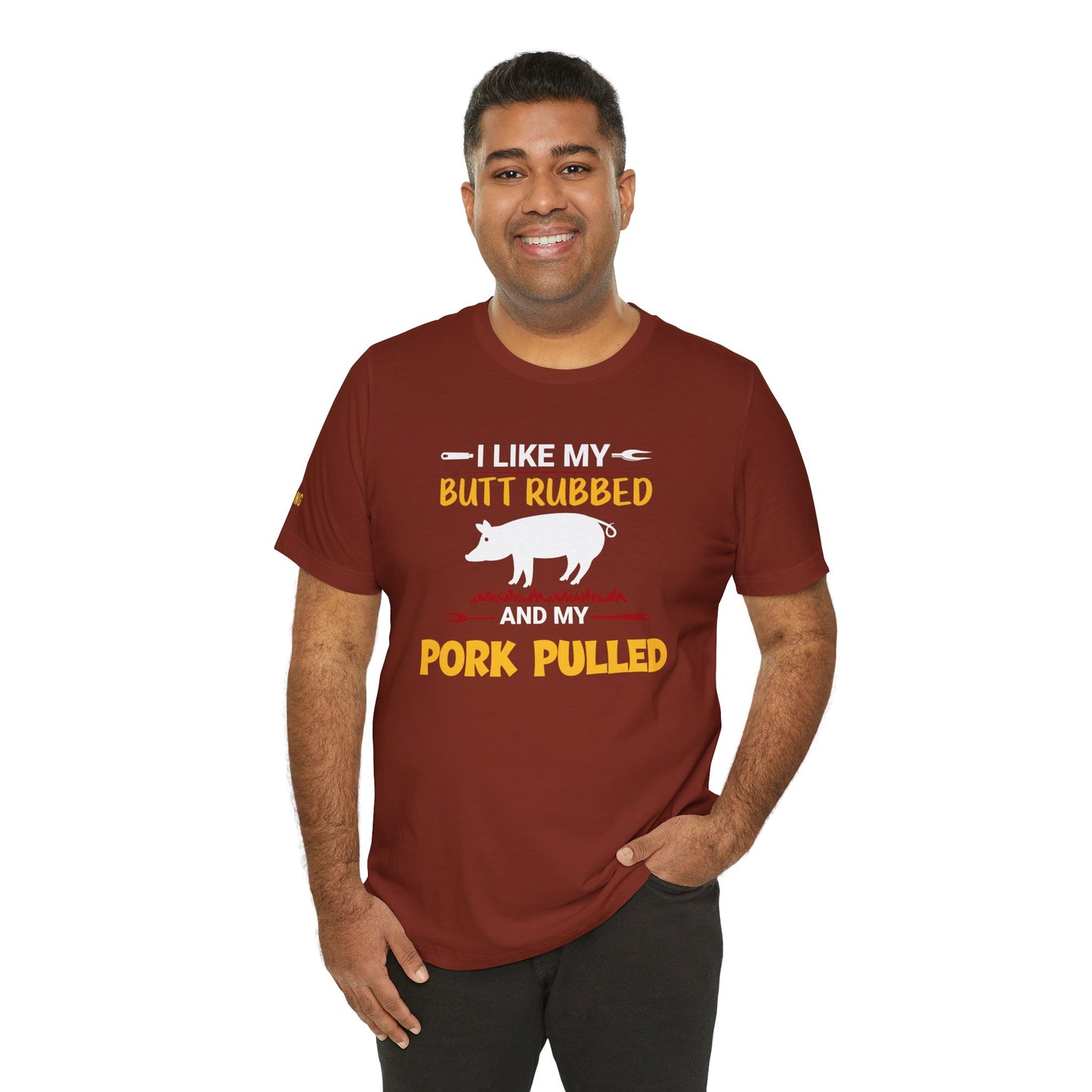 BBQ-themed t-shirt design featuring the phrase "I Like My Butt Rubbed & My Pork Pulled" with a pig silhouette, grill forks, and fire accents.