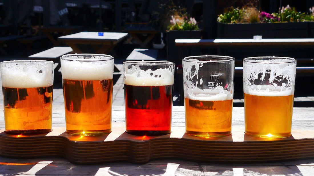A flight of five craft beers, showcasing a range of IPAs from golden and hazy to deep amber, served on a wooden paddle at an outdoor brewery patio.
