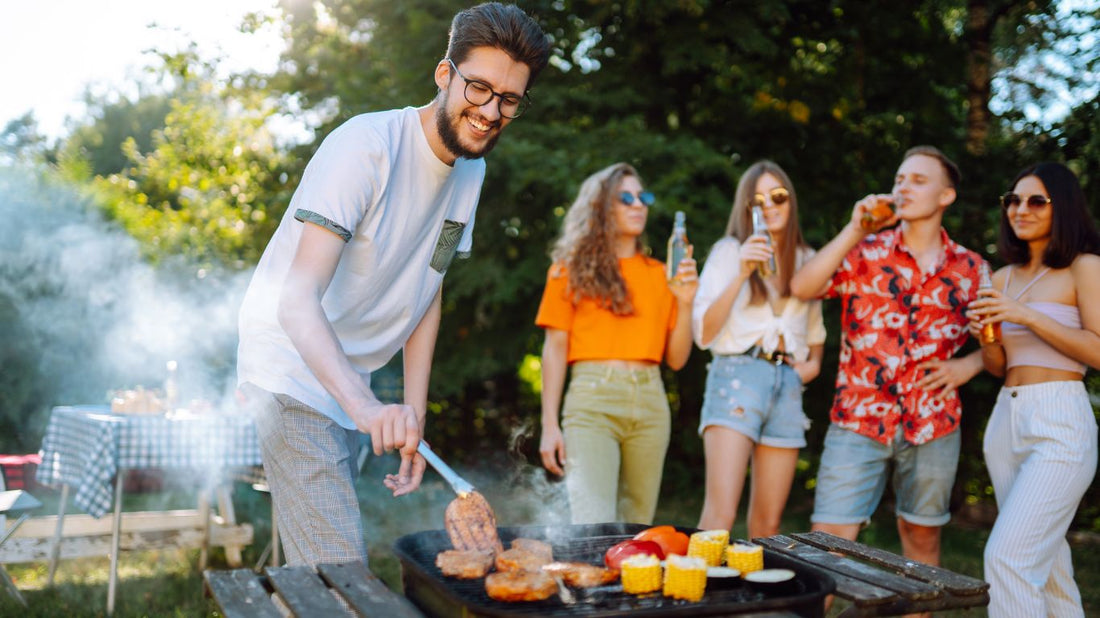 A group of friends enjoying a backyard BBQ with cold beers in hand. A man is grilling steaks and corn on the cob while others socialize, capturing the perfect summer cookout vibe.