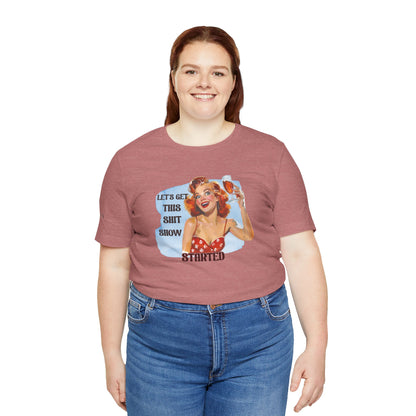Vintage pin-up woman with bright red hair, holding a glass of wine with a manic smile. The phrase reads: "Let’s Get This Sh*t Show Started." - in plus sizes.