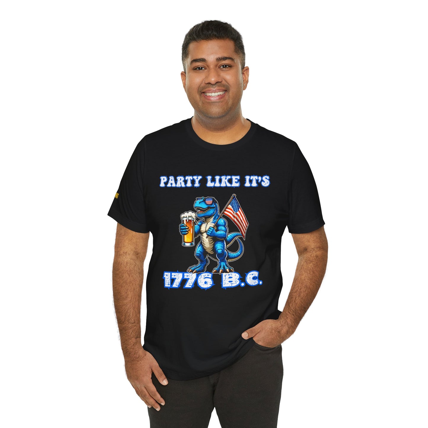 Illustration of a blue T-Rex wearing American flag sunglasses, holding a frosty beer, and waving a USA flag. Funny alcohol quote reads: “Party Like It’s 1776 B.C.” in a bold patriotic font. In black and plus sizes.
