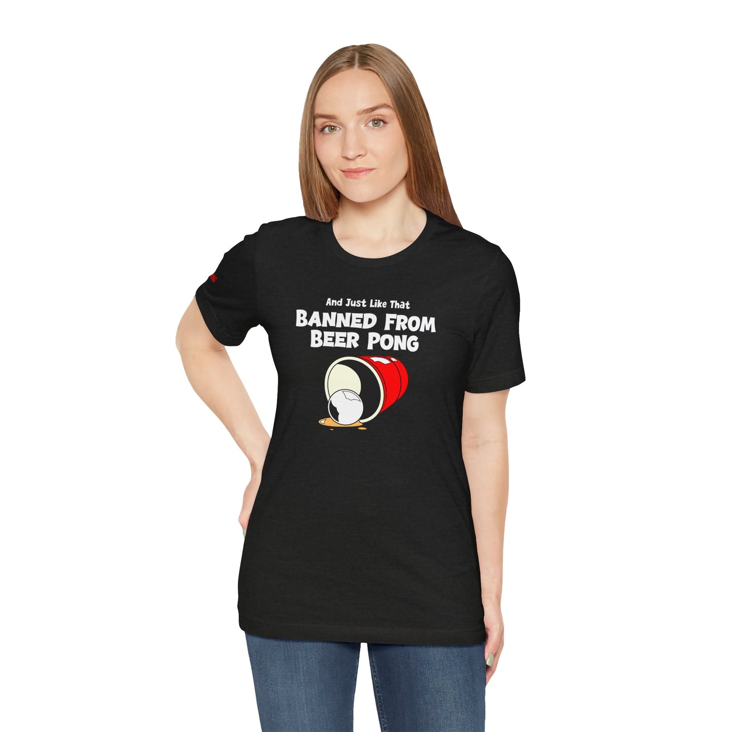 Funny beer pong t-shirt featuring a spilled red party cup and beer pong ball. The text reads “And Just Like That, Banned from Beer Pong” in a bold, playful font.