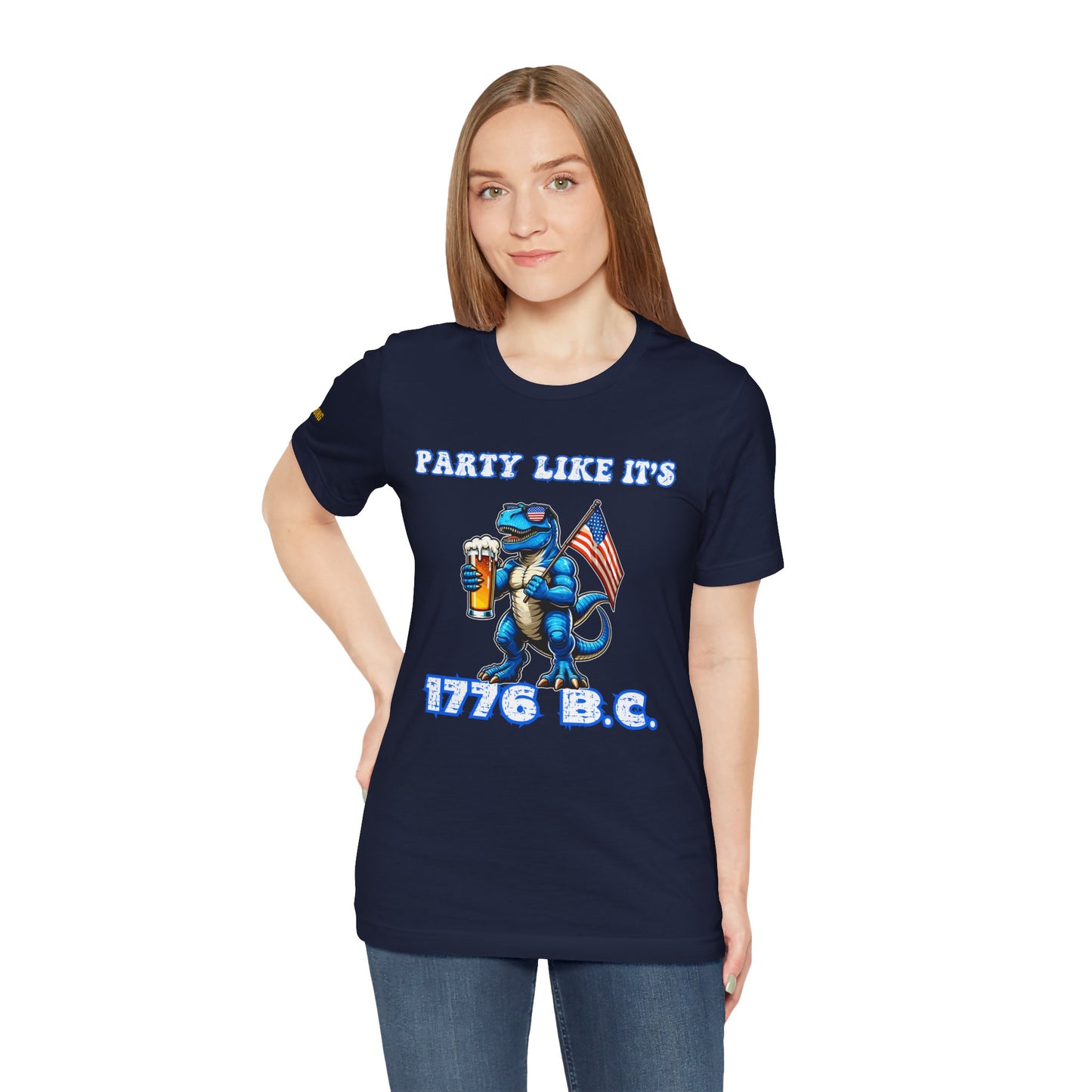 Illustration of a blue T-Rex wearing American flag sunglasses, holding a frosty beer, and waving a USA flag. Funny alcohol quote reads: “Party Like It’s 1776 B.C.” in a bold patriotic font. Navy and plus sizes.