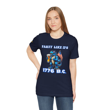 Illustration of a blue T-Rex wearing American flag sunglasses, holding a frosty beer, and waving a USA flag. Funny alcohol quote reads: “Party Like It’s 1776 B.C.” in a bold patriotic font. Navy and plus sizes.
