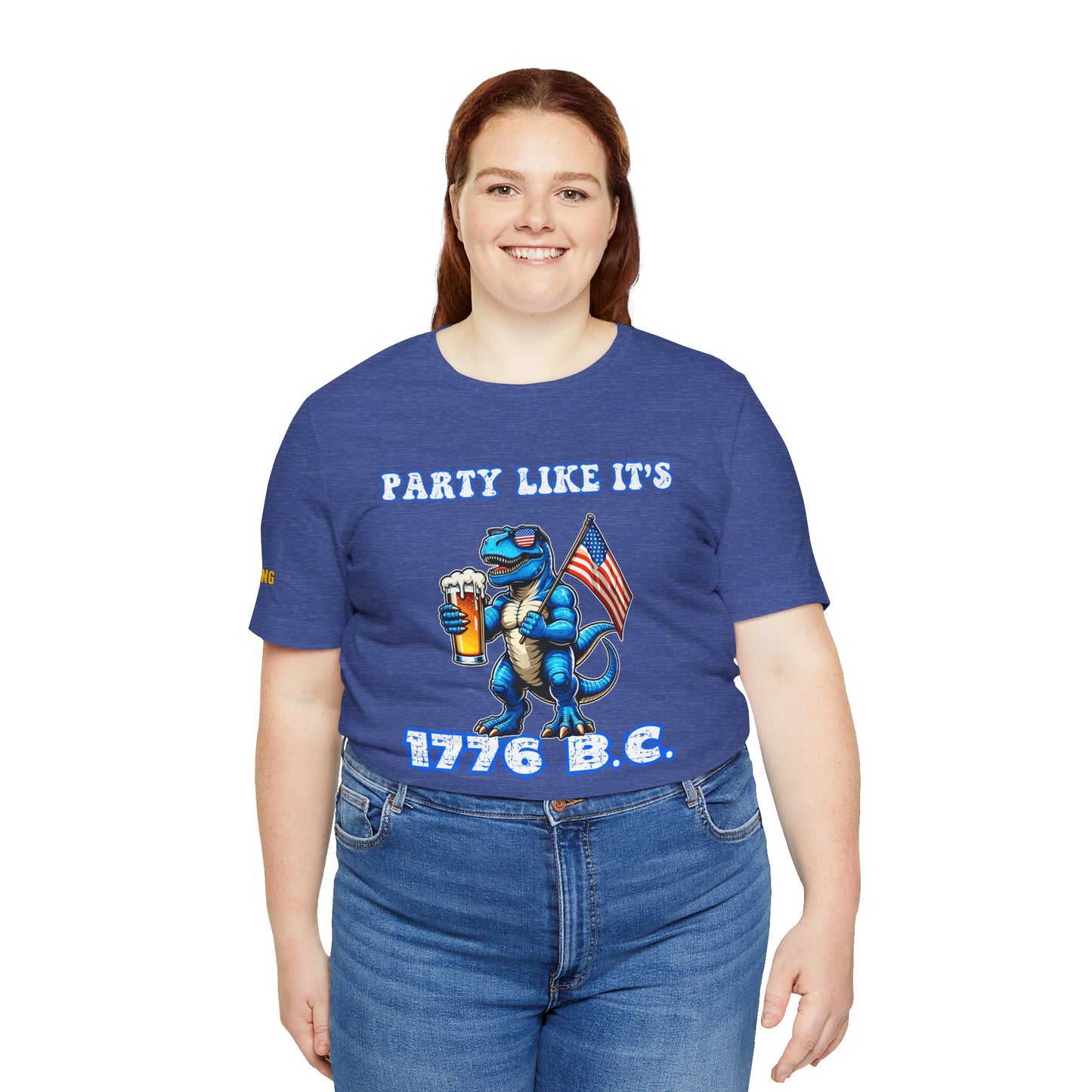 Illustration of a blue T-Rex wearing American flag sunglasses, holding a frosty beer, and waving a USA flag. Funny alcohol quote reads: “Party Like It’s 1776 B.C.” in a bold patriotic font. Heather royal and plus sizes.