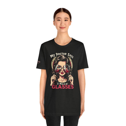 Illustration of a stylish woman holding two red wine glasses as eyeglasses, with bold text reading “My Doctor Says I Need Glasses.” A perfect funny wine t-shirt for moms, wine lovers, and brunch enthusiasts.