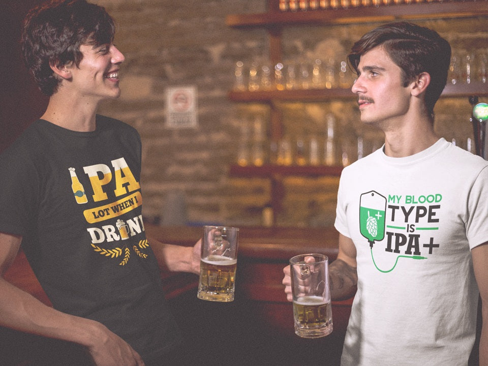 Two men holding beer in a dark lit bar. Both wearing Beer Strong IPA design t-shirts, one "IPA lot when I drink" and the other "My blood type is IPA+". Funny alcohol quote designs.