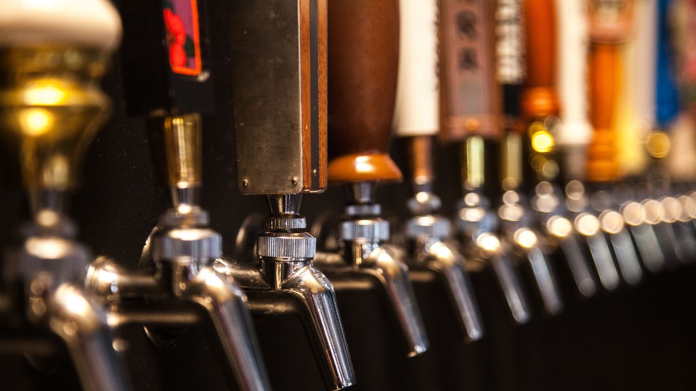 A wall of beer taps lined up and ready to pour, representing the massive selection of Beer Strong tees and hoodies on tap. Just like craft beer, our apparel is brewed for comfort, style, and endless variety. Find your perfect pour!