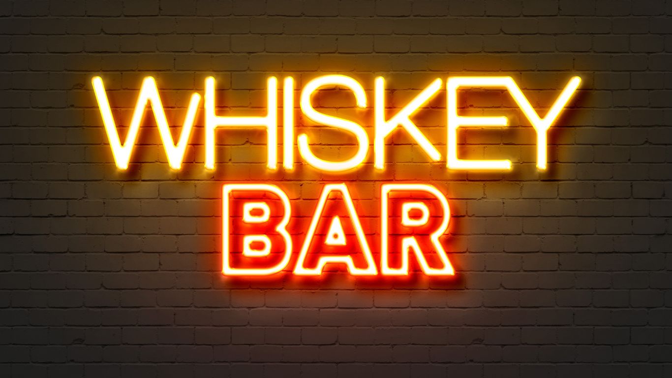 Neon whiskey bar sign with bold glowing text, representing a collection of whiskey-themed t-shirts featuring quotes, humor, and designs for true whiskey lovers.